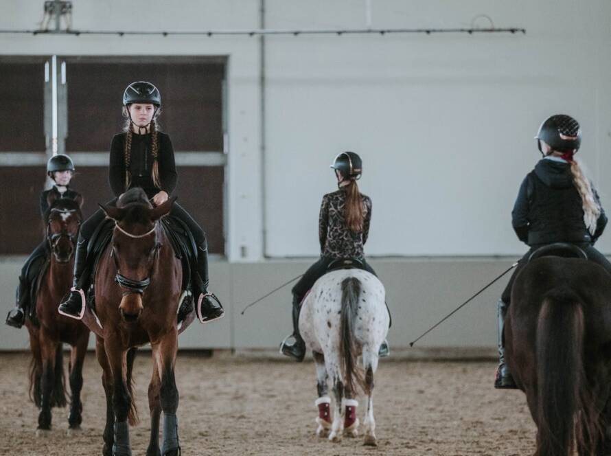 Vier Mädchen reiten auf ihren Pferden, während sie eine Reitstunde nehmen.