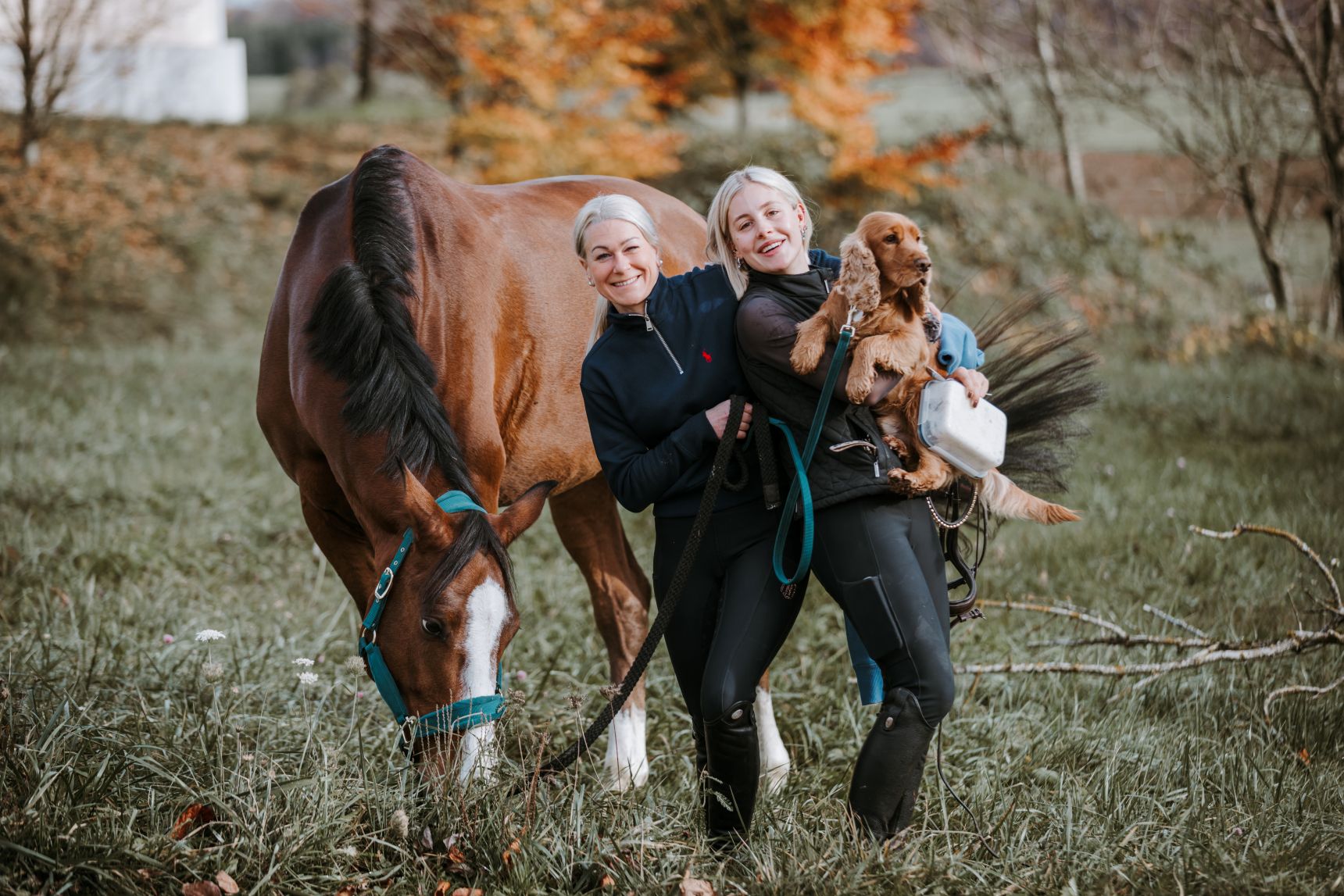 Zwei Reiterinnen, die auf dem grünen Hof mit Pferd und Hund stehen.